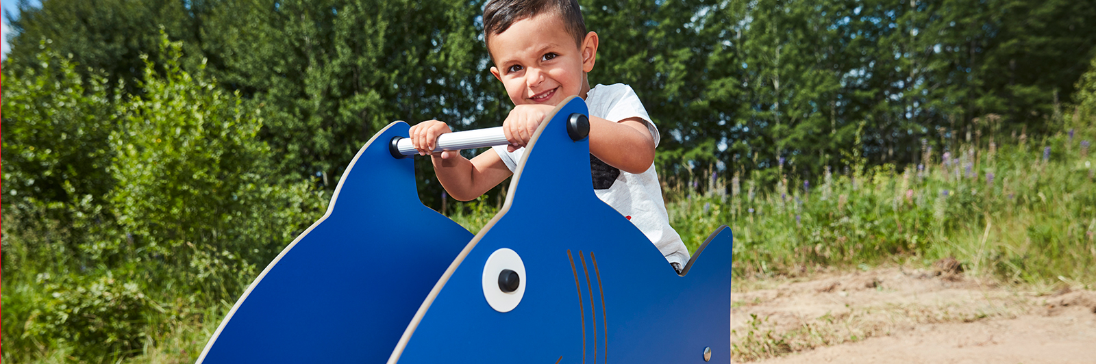 A young boy smiles at the camera while rocking on a shark themed spring toy